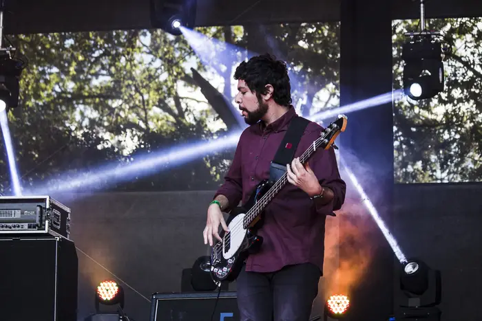 Guitarrista em palco ao ar livre, com árvores ao fundo