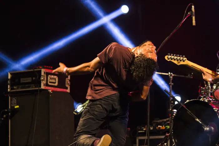 Músico dobrado sobre o instrumento, em palco com feixes de luz