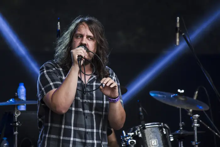 Vocalista de camisa aos quadrados a cantar, sob luz azul