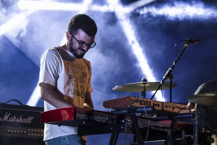 Teclista em palco, rodeado de luz e fumo