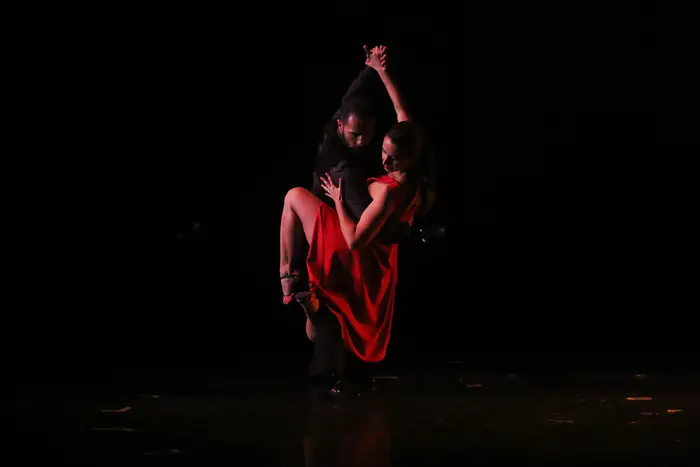 Par de dança em palco escuro, com um foco de luz quente