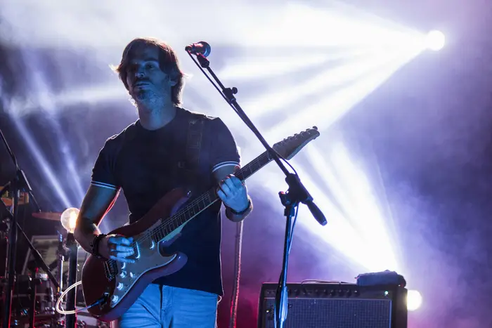 Guitarrista em contraluz, com feixes de luz a cruzar o palco