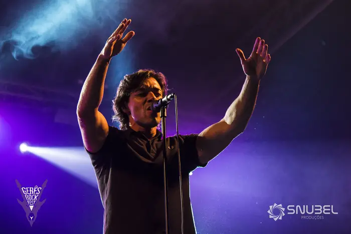Vocalista em palco, de braços erguidos, sob luz azul