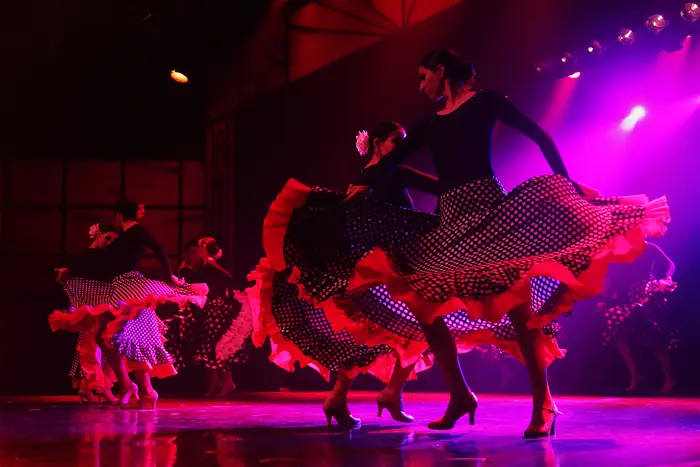 Grupo de bailarinas com saias rodadas, em palco com luz vermelha e magenta