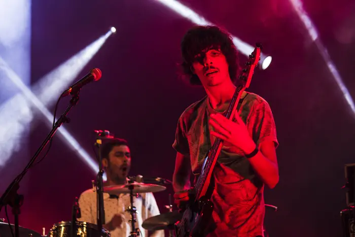 Guitarrista em palco sob luz vermelha, com baterista ao fundo