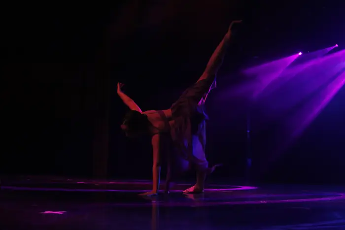 Bailarino num movimento acrobático, em palco iluminado a violeta