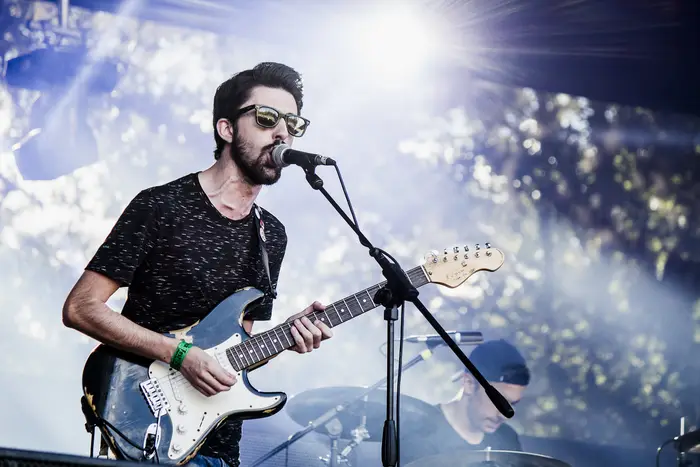 Guitarrista a cantar ao microfone, com árvores e luz de palco ao fundo