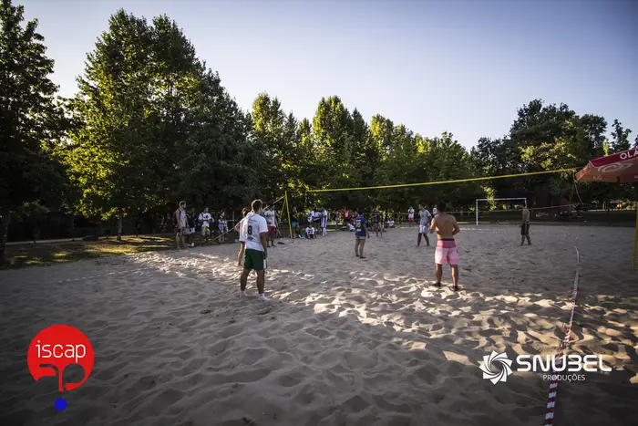 Pessoas a jogar voleibol num areal junto ao rio, num dia de sol