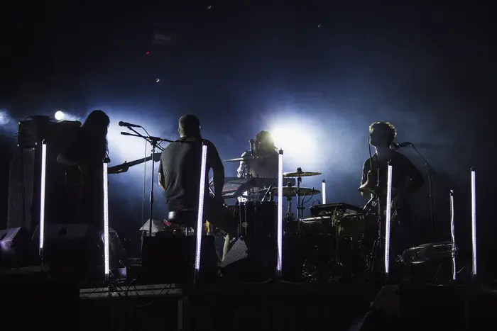 Banda em palco vista em silhueta, com luzes ao fundo
