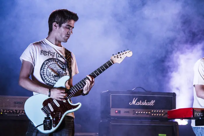 Guitarrista de t-shirt branca com guitarra azul-clara em palco