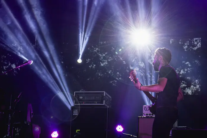 Guitarrista em contraluz, entre feixes de luz azul e violeta