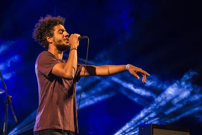 Vocalista de cabelo encaracolado a cantar, de braço estendido