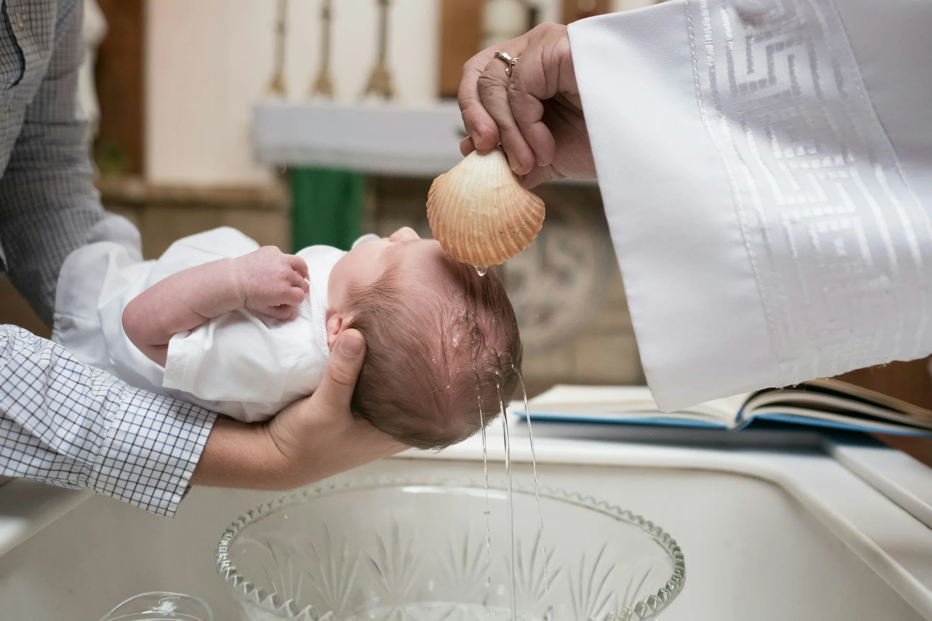 Sacerdote derrama água benta com uma concha sobre a cabeça de um bebé durante o batizado