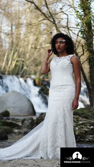 Retrato de uma noiva de vestido branco junto a uma cascata, num bosque